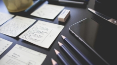 A creative workspace featuring UI design plans, pencils, a smartphone, and other office tools.