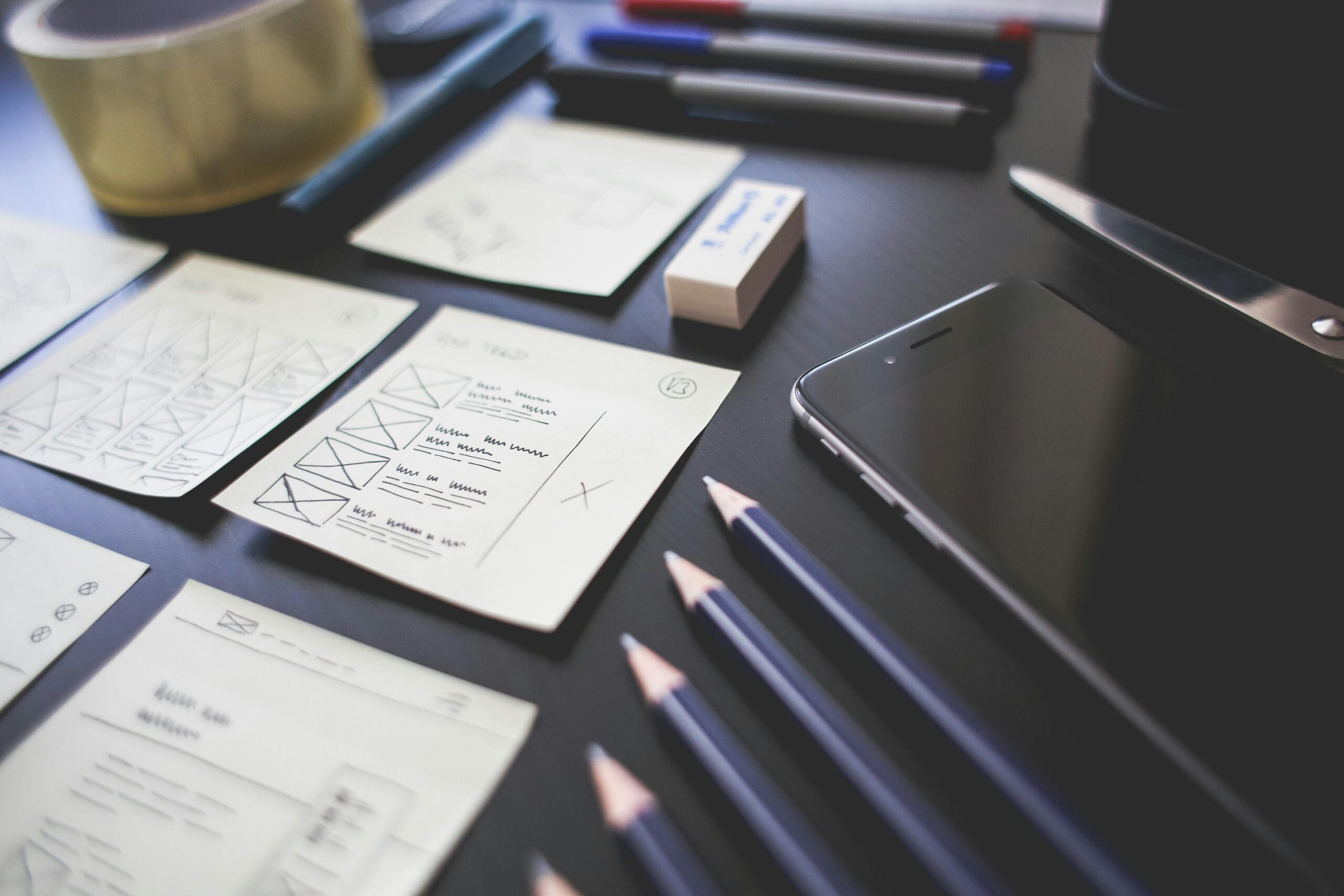 A creative workspace featuring UI design plans, pencils, a smartphone, and other office tools.